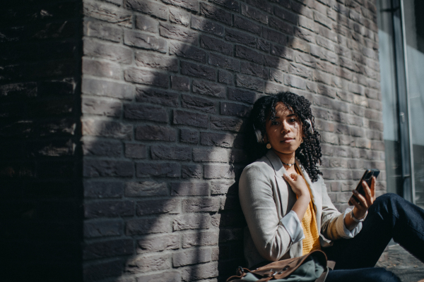 A young biracial woman wearing headphones and enjoying listening to music outdoors in street.