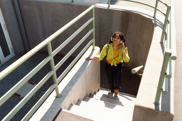 A young biracial woman wearing headphones and enjoying listening to music outdoors in street.