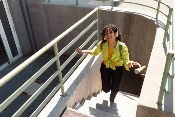 A young biracial woman wearing headphones and enjoying listening to music outdoors in street.