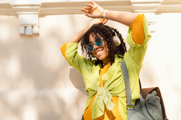 A young biracial woman wearing headphones and enjoying listening to music outdoors in street.