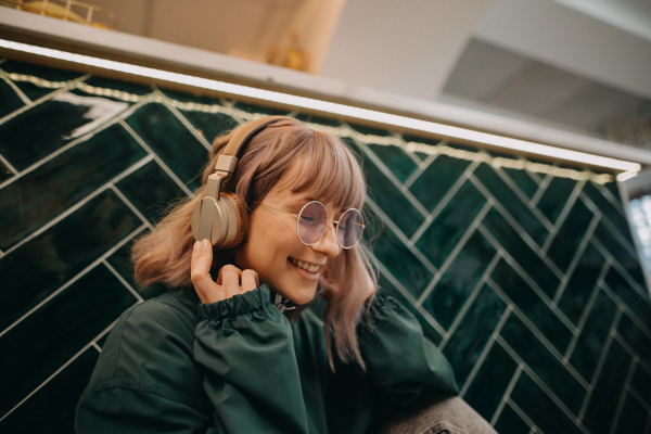 A young woman wearing headphones and enjoying listening to music indoors.