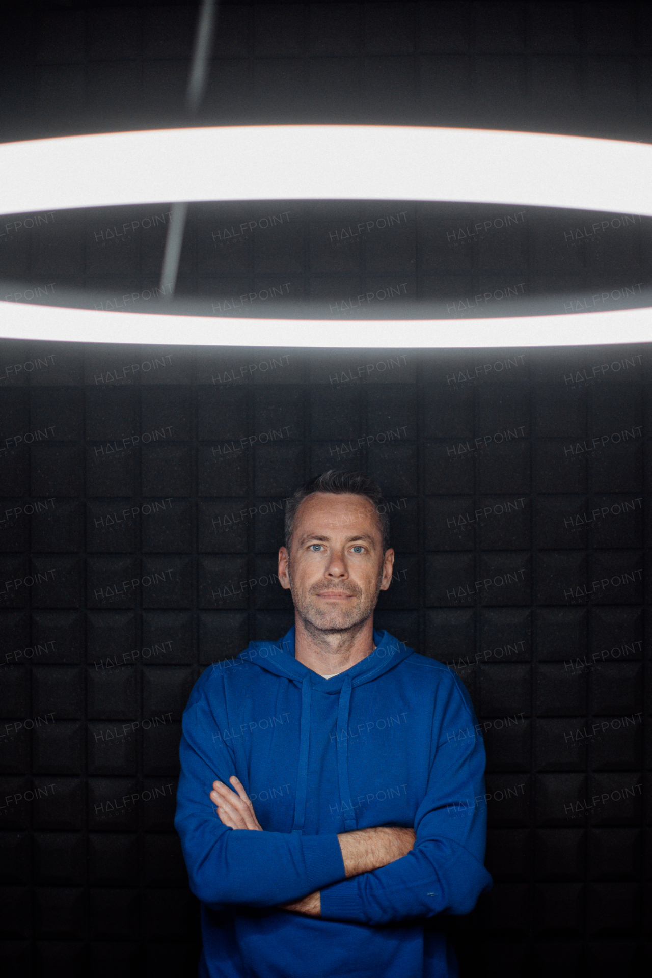 A portrait of happy mature man with arms crossed standing in studio with dark background and looking at camera.