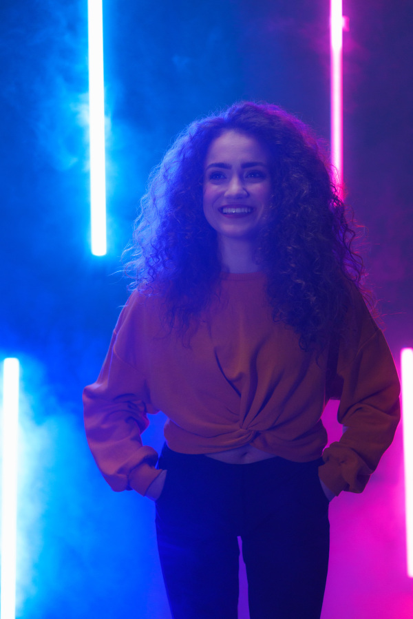 A modern dance girl dancer dancing in neon light doing gymnastic exercises in studio, copy space.