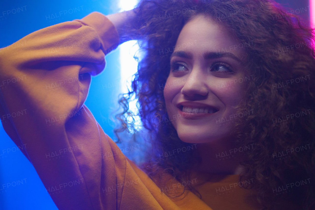 A portrait of a happy young woman dancing over neon light background at disco party