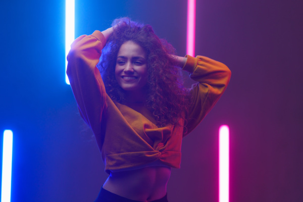 A portrait of a happy young woman dancing over neon light background at disco party