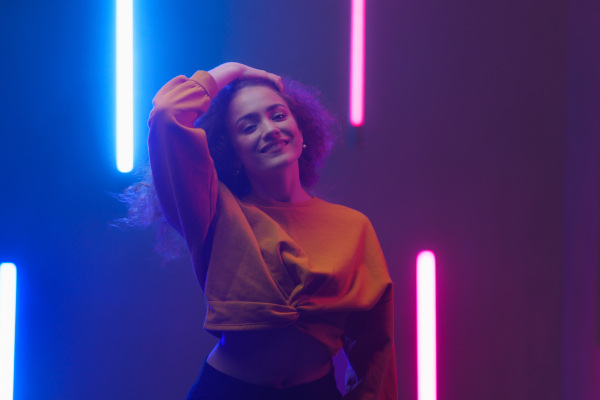 A portrait of a happy young woman dancing over neon light background at disco party