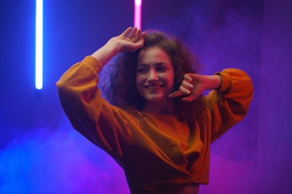 A portrait of a happy young woman dancing over neon light background at disco party