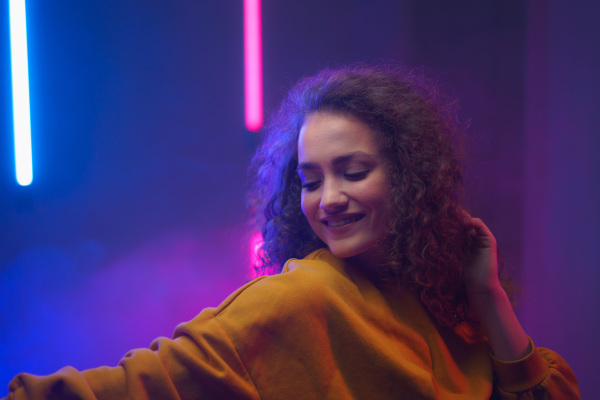 A portrait of a happy young woman dancing over neon light background at disco party