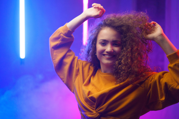 A portrait of a happy young woman dancing over neon light background at disco party