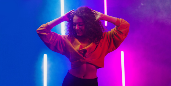 A portrait of a happy young woman dancing over neon light background at disco party