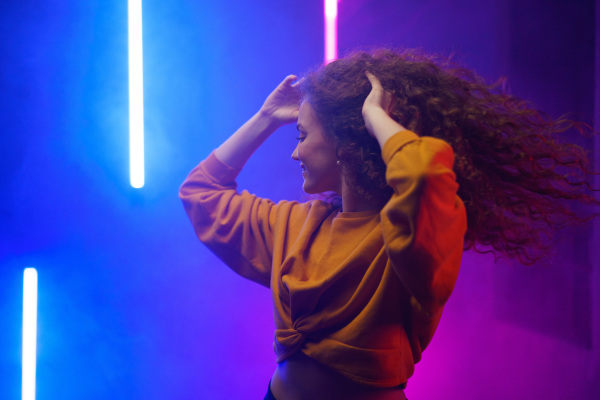 A portrait of a happy young woman dancing over neon light background at disco party