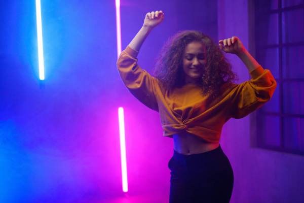 A portrait of a happy young woman dancing over neon light background at disco party