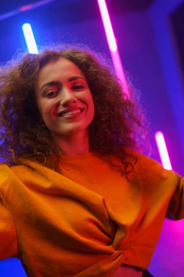 A portrait of a happy young woman dancing over neon light background at disco party