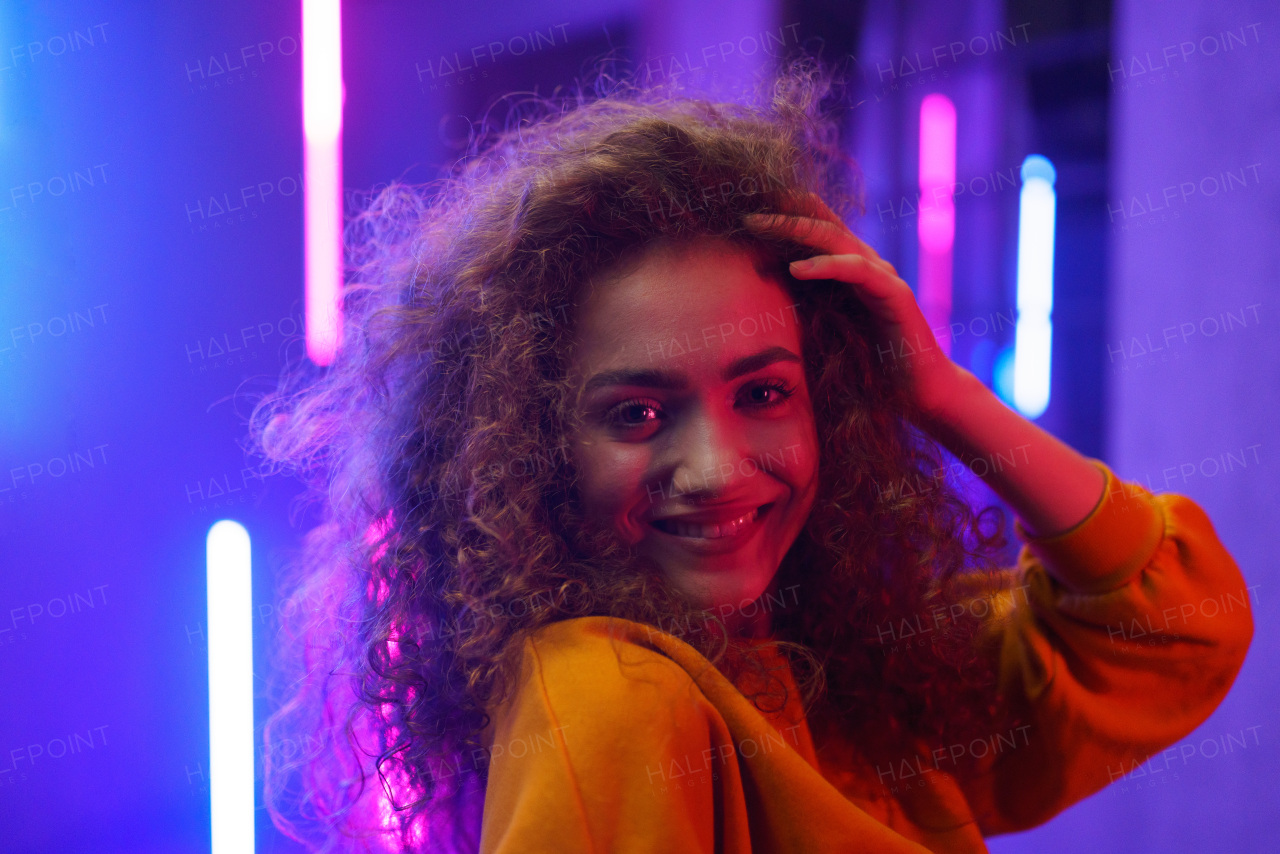 A portrait of a happy young woman dancing over neon light background at disco party