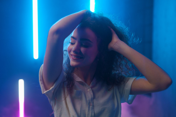 A portrait of a happy young woman dancing over neon light background at disco party