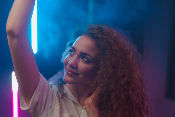 A portrait of a happy young woman dancing over neon light background at disco party