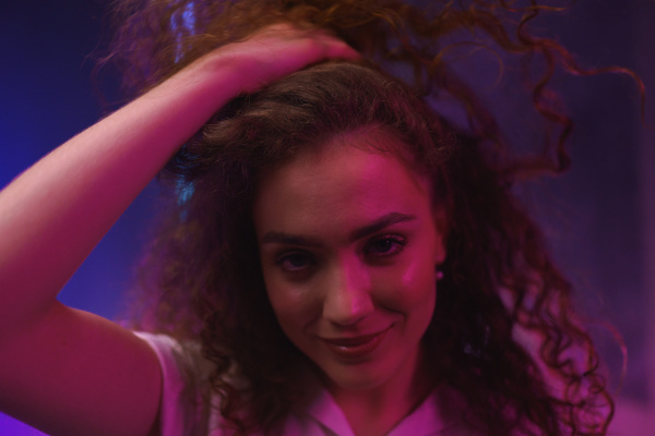 A portrait of a happy young woman dancing over neon light background at disco party