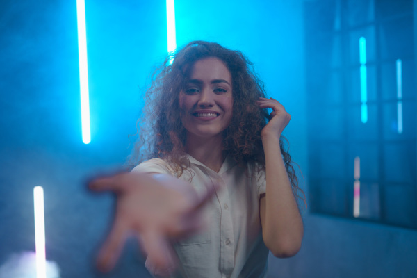 A portrait of a happy young woman invitating to come and looking at camera over neon light background