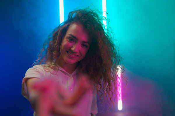 A portrait of a happy young woman invitating to come and looking at camera over neon light background