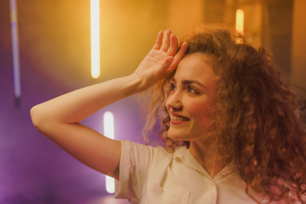 A portrait of a happy young woman dancing over neon light background at disco party