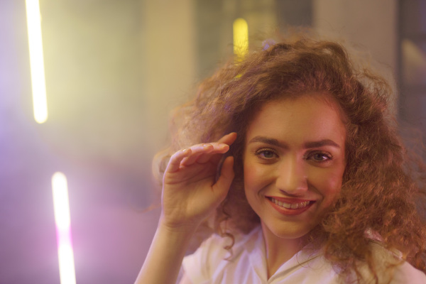 A portrait of a happy young woman dancing over neon light background at disco party