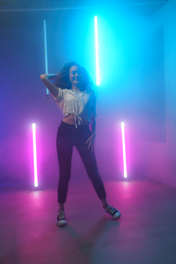 A modern dance girl dancer dancing in neon light doing gymnastic exercises in studio, copy space.