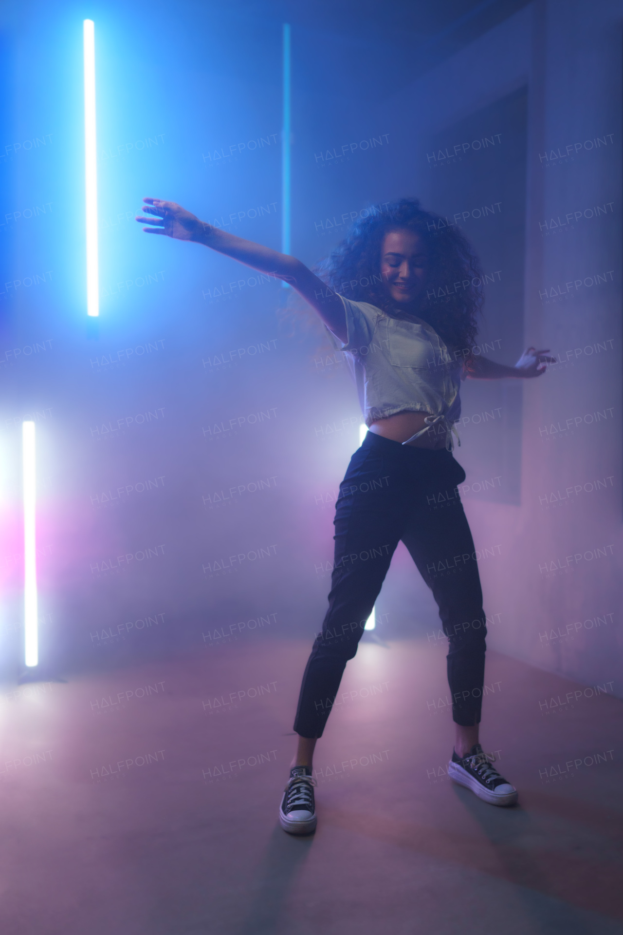 A modern dance girl dancer dancing in neon light doing gymnastic exercises in studio, copy space.