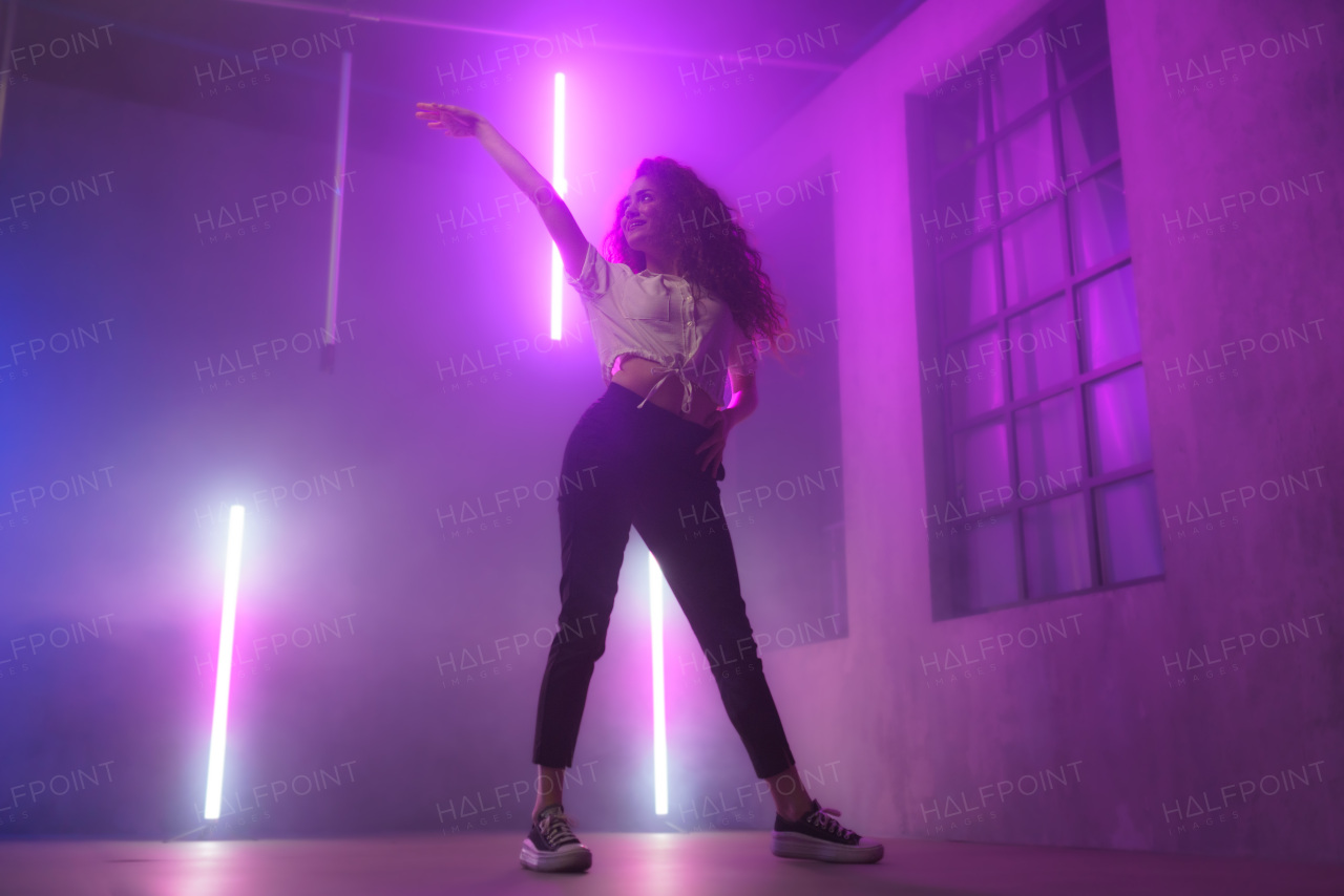 A modern dance girl dancer dancing in neon light doing gymnastic exercises in studio, copy space.