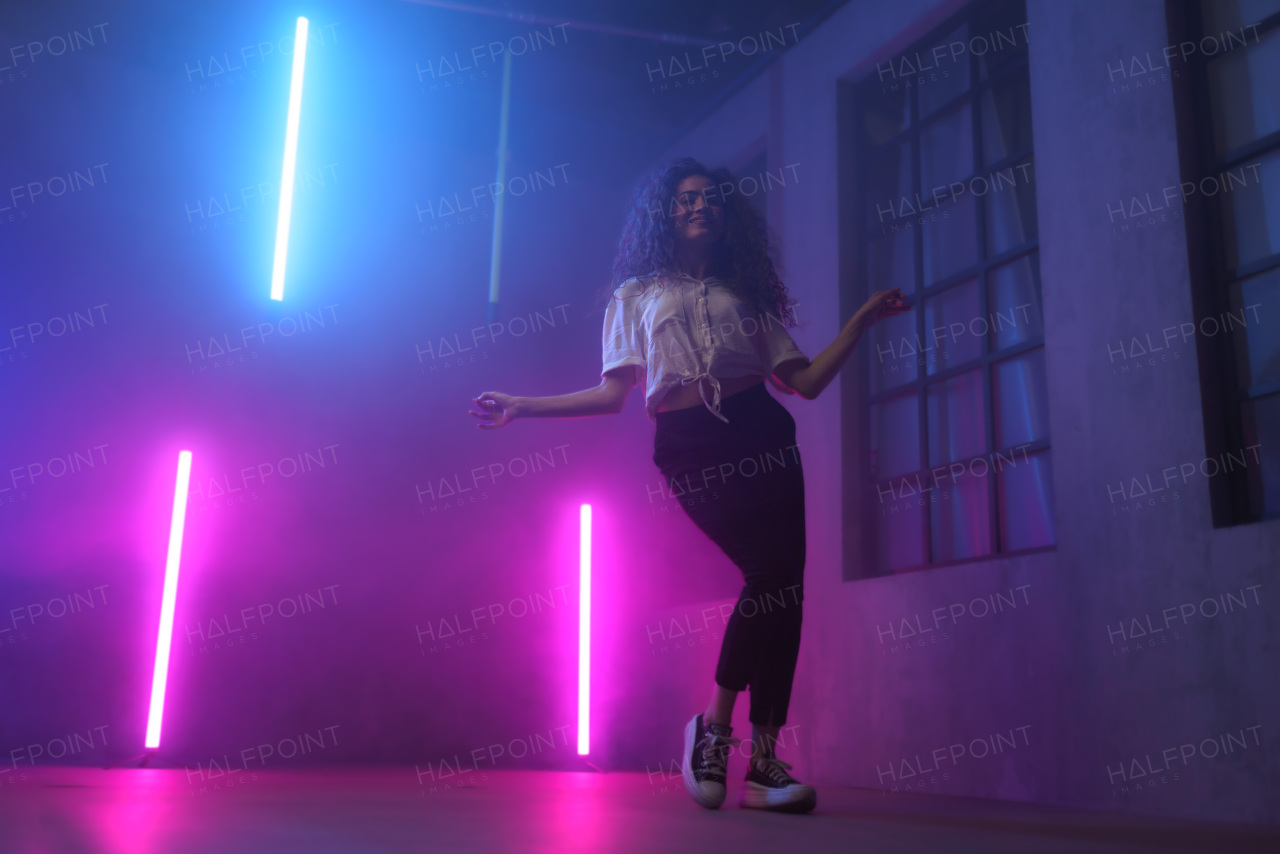 A portrait of a happy young woman dancing over neon light background at disco party