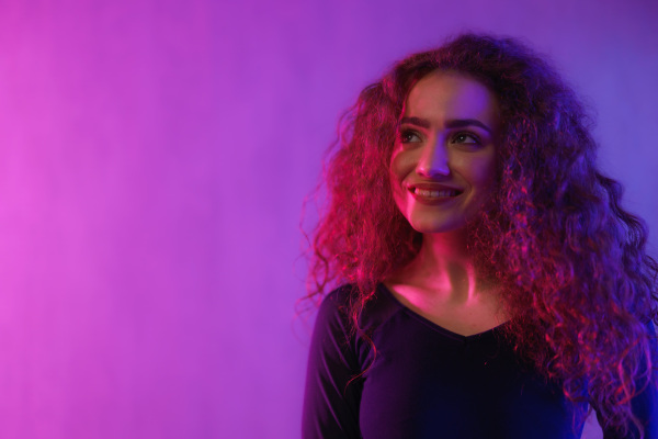 A portrait of a happy young woman dancing over neon light background at disco party