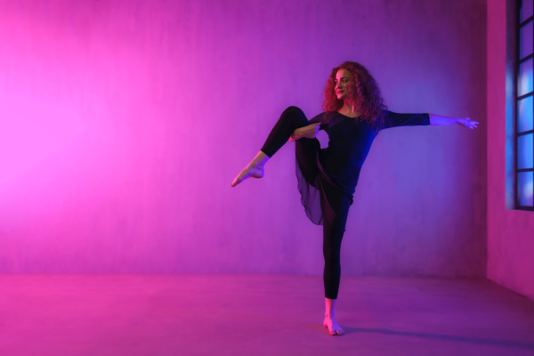 A modern dance girl dancer dancing in neon light doing gymnastic exercises in studio, copy space.