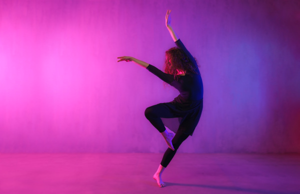 A modern dance girl dancer dancing in neon light doing gymnastic exercises in studio, copy space.