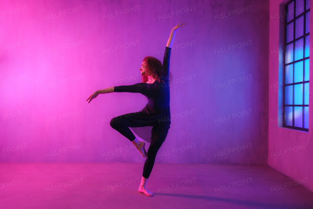 A modern dance girl dancer dancing in neon light doing gymnastic exercises in studio, copy space.