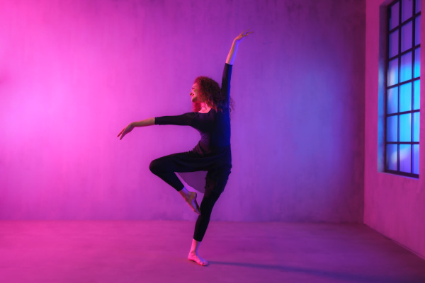 A modern dance girl dancer dancing in neon light doing gymnastic exercises in studio, copy space.