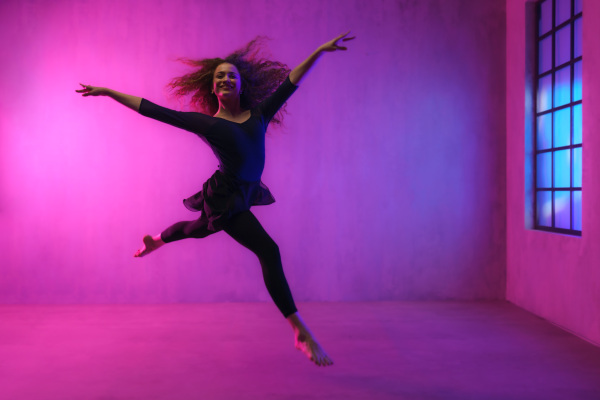 A modern dance girl dancer dancing in neon light doing gymnastic exercises in studio, copy space.