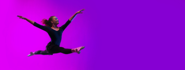 A m odern dance girl dancer jumping up dancing in neon light doing gymnastic exercises in studio, wide banner, copy space.