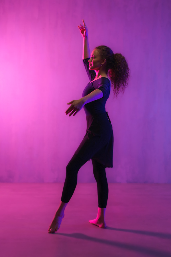 A modern dance girl dancer dancing in neon light doing gymnastic exercises in studio, copy space.