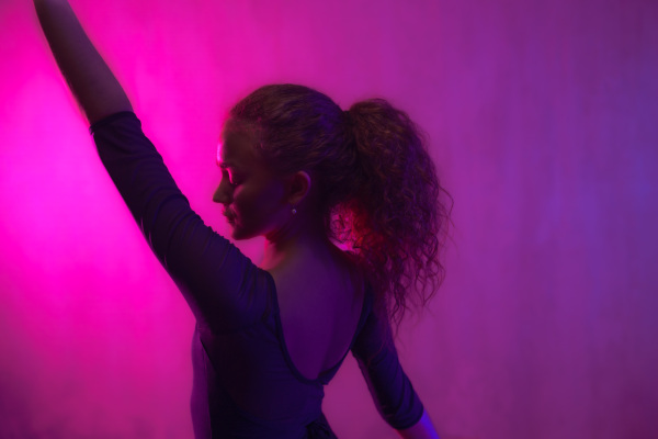 A ballet girl dancer dancing in neon light doing gymnastic exercises in studio, copy space.