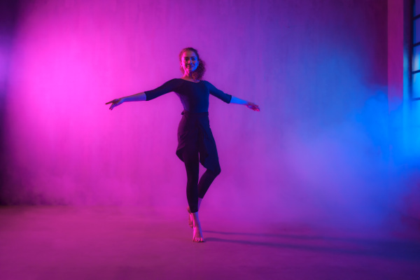 A modern dance girl dancer dancing in neon light doing gymnastic exercises in studio, copy space.