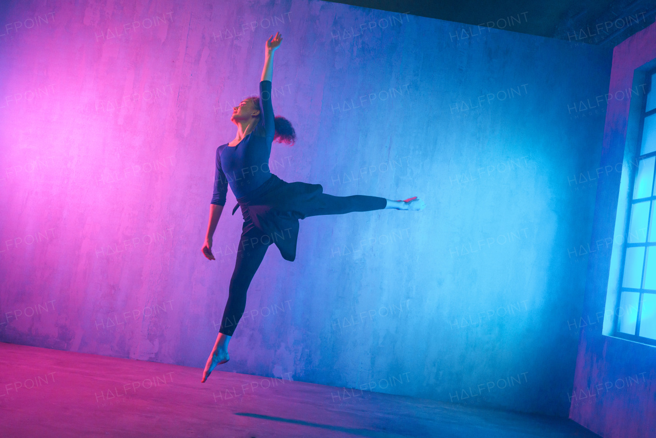 A modern dance girl dancer dancing in neon light doing gymnastic exercises in studio, copy space.