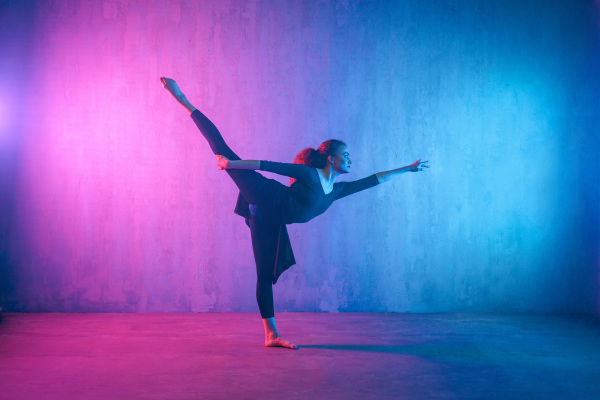 A modern dance girl dancer dancing in neon light doing gymnastic exercises in studio, copy space.