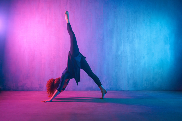 A modern dance girl dancer dancing in neon light doing gymnastic exercises in studio, copy space.