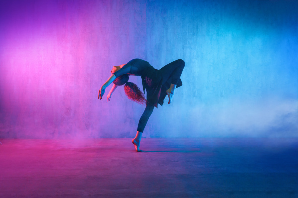 A modern dance girl dancer dancing in neon light doing gymnastic exercises in studio, copy space.