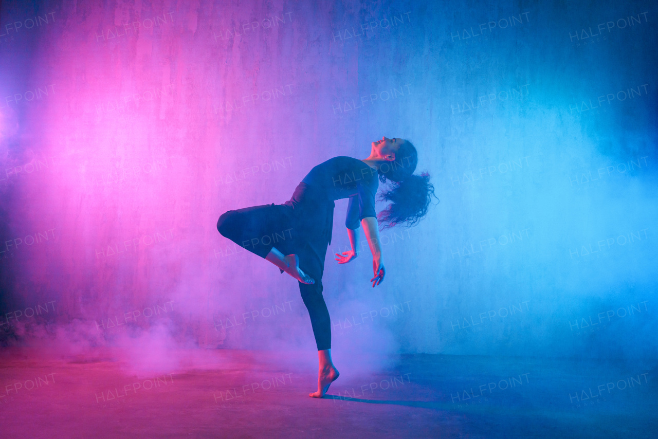 A modern dance girl dancer dancing in neon light doing gymnastic exercises in studio, copy space.