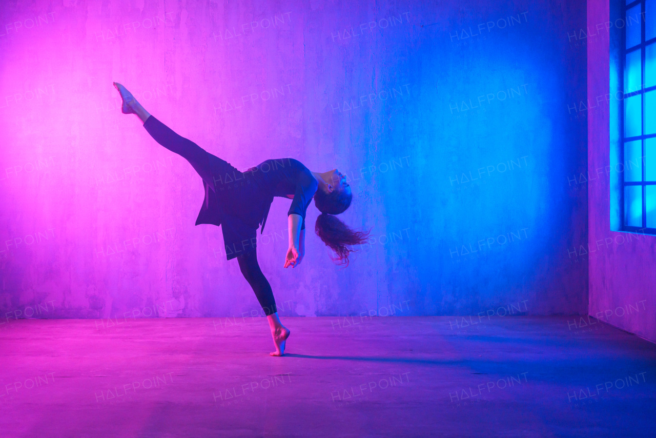 A modern dance girl dancer dancing in neon light doing gymnastic exercises in studio, copy space.