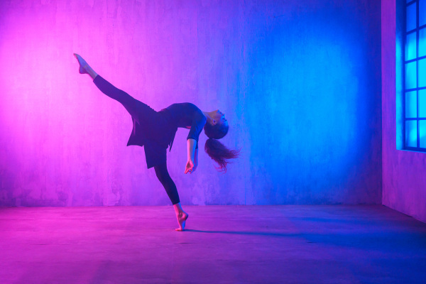 A modern dance girl dancer dancing in neon light doing gymnastic exercises in studio, copy space.