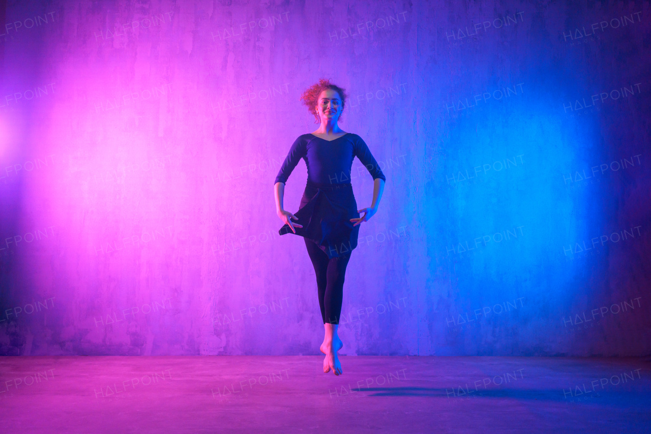 A modern dance girl dancer dancing in neon light doing gymnastic exercises in studio, copy space.