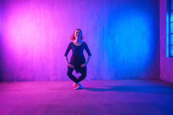 A modern dance girl dancer dancing in neon light doing gymnastic exercises in studio, copy space.