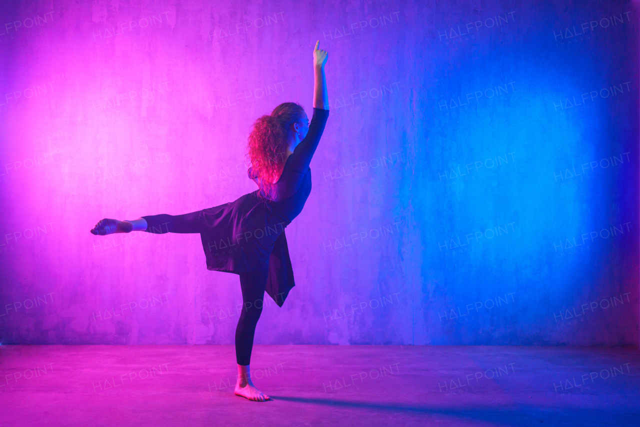 A modern dance girl dancer dancing in neon light doing gymnastic exercises in studio, copy space.