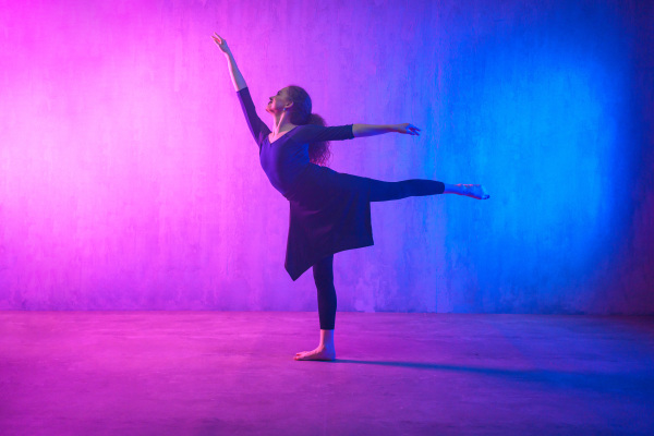 A modern dance girl dancer dancing in neon light doing gymnastic exercises in studio, copy space.